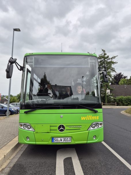 Grüner Bus steht an einer Haltestelle unter einem bewölkten Himmel.