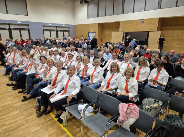 Gruppensitzung mit vielen Menschen in weißen Hemden und orangefarbenen Krawatten.